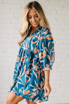 Blonde woman wearing a 3/4 sleeves leaf print dress with front tie neck detail, ruffled neckline, side pockets.