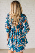 Blonde woman wearing a 3/4 sleeves leaf print dress with front tie neck detail, ruffled neckline, side pockets.