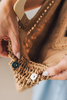 Blonde woman in blue dress holding an oversized rectangle straw tote with wood handles.