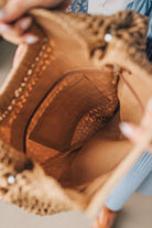 Blonde woman in blue dress holding an oversized rectangle straw tote with wood handles.