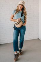 Blonde woman in blue shirt wearing a tan crossbody bag with black zippers.