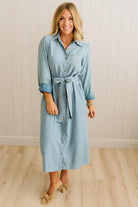 Woman wearing a light blue dress with a belt against a white paneled wall.