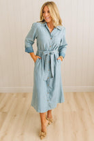 Woman wearing a light blue denim dress with a belt in a minimalistic setting.