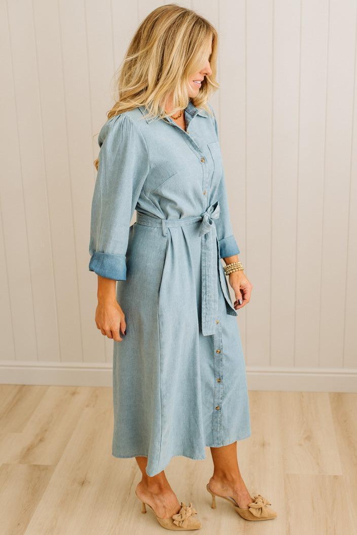 Woman wearing a light blue dress with a belt against a neutral background