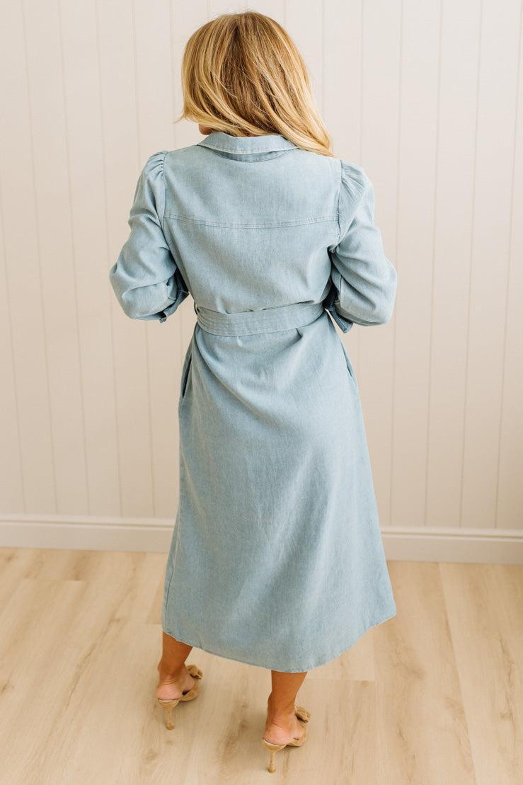 Woman wearing a light blue dress with a belt in a minimal indoor setting
