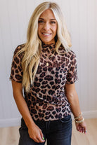 Woman wearing a leopard print top and black pants against a plain background