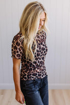 Woman wearing a leopard print shirt and blue jeans against a plain background