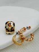 Pair of earrings, one with leopard print design and the other gold hoop, on a white surface.