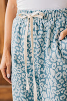 BLONDE WOMAN WEARING WASHED LEOPARD PATTERN PANTS WQITH CURVED SIDE SEAM AND WITH DRAWSTRING WAIST.