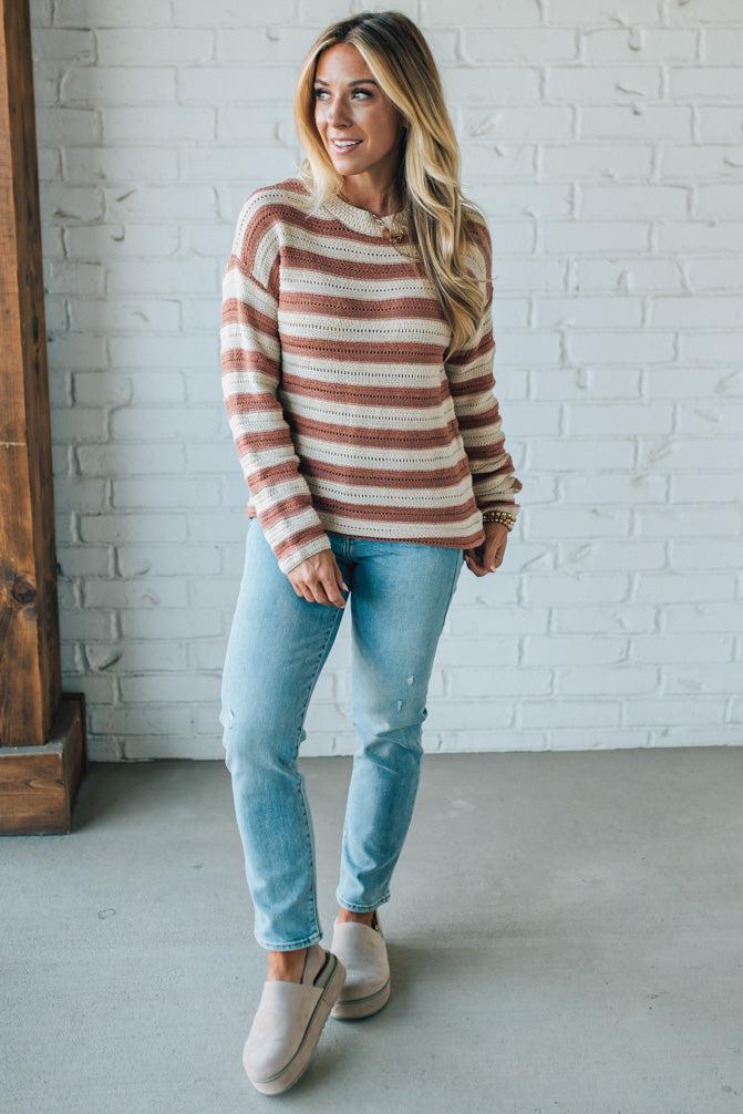Woman wearing a striped sweater and jeans standing against a white brick wall.