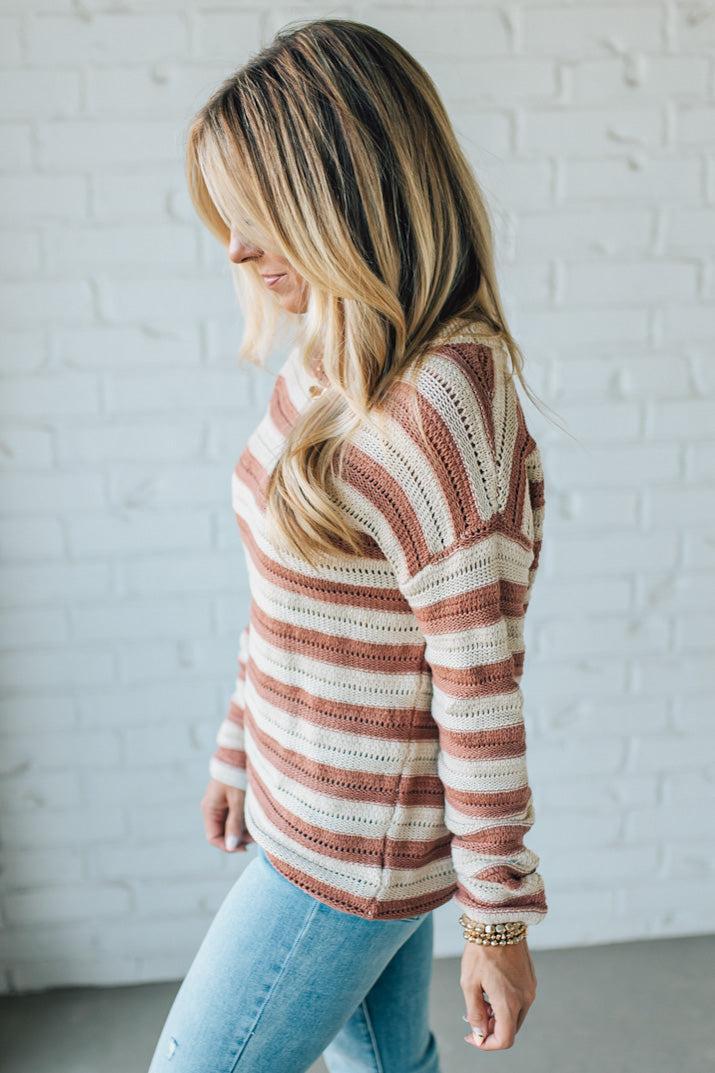 Woman wearing a striped sweater and jeans against a white brick wall.