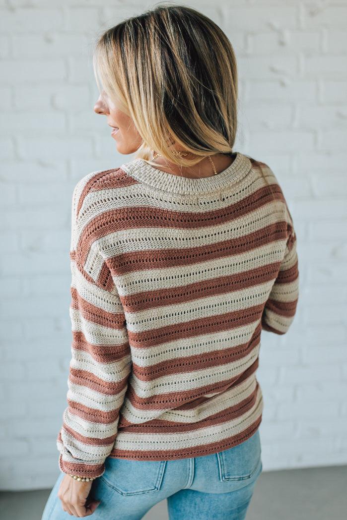 Woman wearing a striped sweater and jeans against a white brick wall.