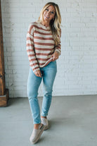 Woman wearing a striped sweater and jeans standing against a white brick wall.