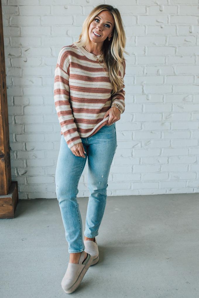 Woman wearing a striped sweater and jeans standing against a white brick wall.