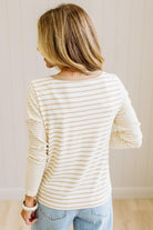 Blonde woman in a brightly lit studio wearing light wide leg jeans, dark clogs, and a striped henley top in cream and taupe.