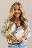 Blonde woman in a brightly lit studio wearing light wide leg jeans, dark clogs, and a striped henley top in cream and charcoal.