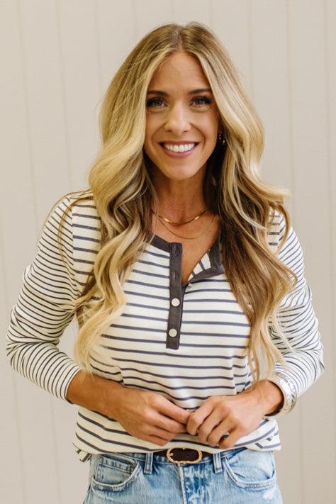 Blonde woman in a brightly lit studio wearing light wide leg jeans, dark clogs, and a striped henley top in cream and charcoal.