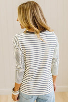 Blonde woman in a brightly lit studio wearing light wide leg jeans, dark clogs, and a striped henley top in cream and charcoal.