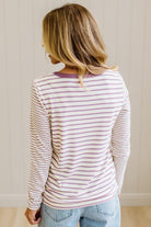 Blonde woman in a brightly lit studio wearing light wide leg jeans, dark clogs, and a striped henley top in cream and lavender.