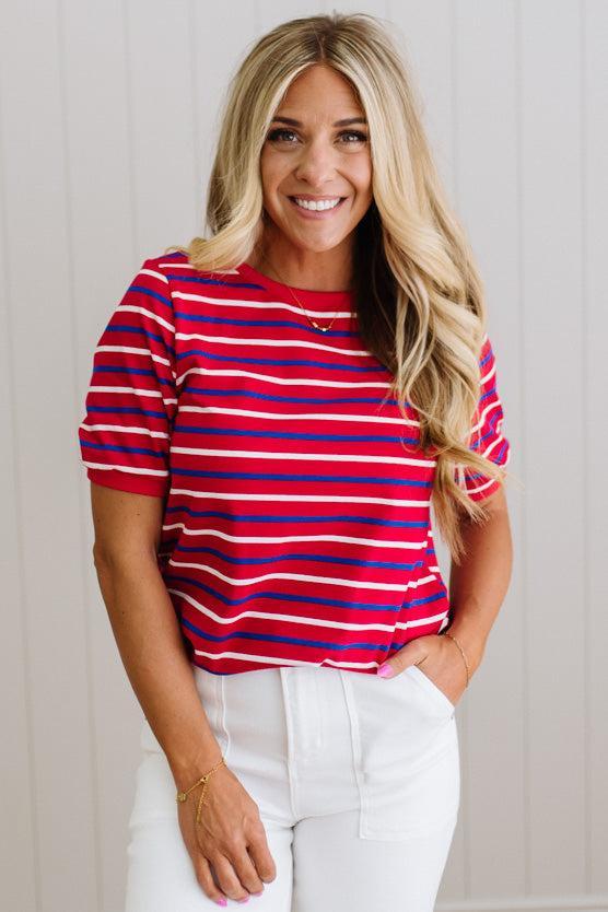 Woman wearing a red and blue striped shirt with white pants against a light background