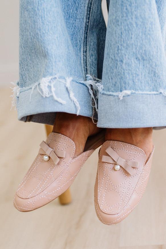 Pink loafers with pearl details worn with light blue jeans on a neutral background