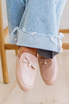 Person wearing pink loafers with pearl embellishments and light blue jeans sitting on a wooden chair.