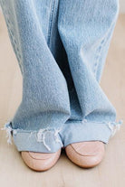 Light blue jeans with frayed cuffs worn by a person on a beige background