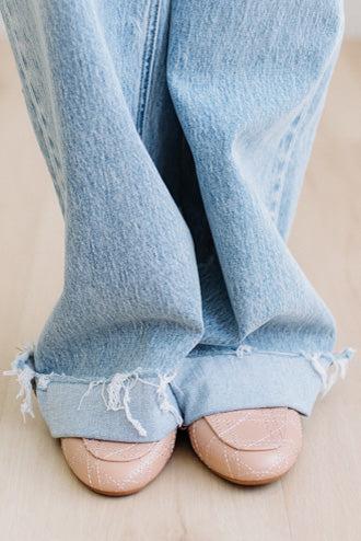 Light blue jeans with frayed cuffs worn by a person on a beige background