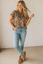 Woman wearing a leopard print top and blue jeans against a white brick wall.