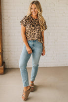 Woman wearing a leopard print top and light blue jeans against a white brick wall.