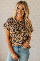 Woman wearing a leopard print top and blue jeans against a white brick wall.