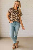 Woman wearing a leopard print top and light blue jeans against a white brick wall.