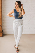 Blonde woman wearing scuba fabric sweatpants with side pockets, a white drawstring on and elastic waistband, and a sewn in center pleat on each leg.