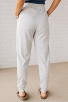 Blonde woman wearing scuba fabric sweatpants with side pockets, a white drawstring on and elastic waistband, and a sewn in center pleat on each leg.