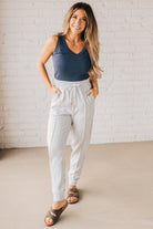 Blonde woman wearing scuba fabric sweatpants with side pockets, a white drawstring on and elastic waistband, and a sewn in center pleat on each leg.