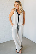 Woman wearing a white sleeveless top and pants with black accents against a white brick wall.
