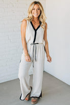 Woman wearing a white sleeveless jumpsuit with black accents against a white brick wall.