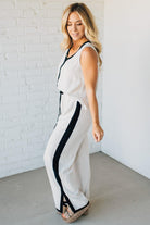 Woman wearing a white sleeveless top and pants with black accents against a white brick wall.