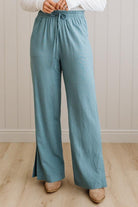 Person wearing teal wide-leg pants with a white top against a neutral background