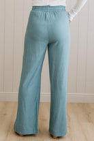 Teal pants worn by a person against a white paneled wall.
