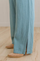 Teal pants with a split design worn by a person on a wooden floor.