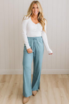 Woman wearing a white long-sleeve top and light blue pants against a neutral background