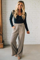 Woman wearing a dark top and light pants standing against a white brick wall.
