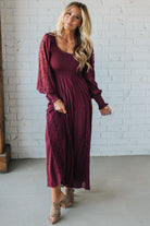 Woman wearing a burgundy dress standing against a white brick wall.