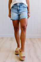 Person wearing denim shorts and sandals on a light wooden floor.