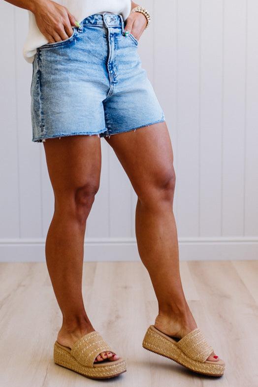 Person wearing denim shorts and sandals on a light wooden floor.