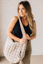 Blonde woman holding an almond color oversized tote with nylon quilted exterior.