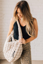 Blonde woman holding an almond color oversized tote with nylon quilted exterior.