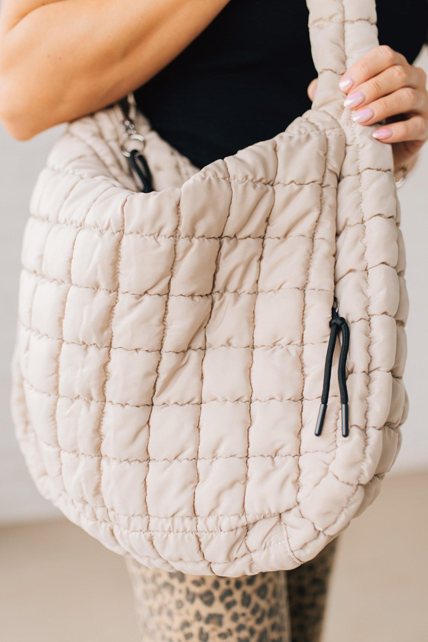 Blonde woman holding an almond color oversized tote with nylon quilted exterior.