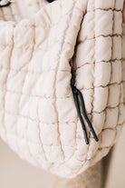 Blonde woman holding an almond color oversized tote with nylon quilted exterior.